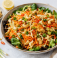 Fresh carrot and cabbage salad served over mixed greens with whole cashews, green onions, Thai peppers, garlic lemon dressing, and sesame oil in a healthy nutrient-rich bowl.