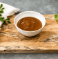 Homemade brown sauce in a white bowl on a rustic wooden serving board